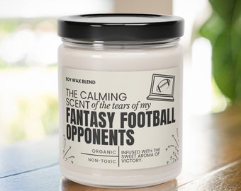 May include: A white soy wax candle with a black lid. The label reads "The Calming Scent of the tears of my Fantasy Football Opponents." It also says "Organic, Non-Toxic" and "Infused with the sweet aroma of victory."