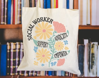 May include: A white canvas tote bag with the words "Social Worker" in a circle around a floral design. The flowers are yellow, pink, and blue. The words "Support", "Advocate", and "Empower" are written on the stems of the flowers.