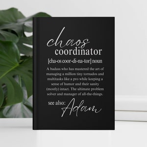 May include: Black notebook with white text that reads "chaos coordinator [cha-os coor-di-na-tor] noun A badass who has mastered the art of managing a million tiny tornados and multitasks like a pro while keeping a sense of humor and their sanity (mostly) intact. The ultimate problem solver and manager of all-the-things. see also: Adam"