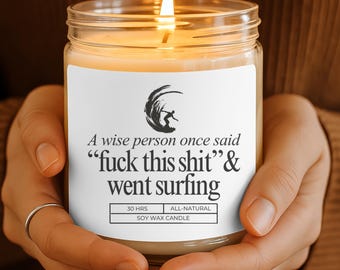 May include: A lit soy wax candle in a glass jar. The label reads "A wise person once said 'fuck this shit' & went surfing." The candle has a burn time of 30 hours and is all-natural.