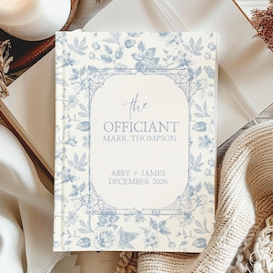 May include: A hardcover book with a floral pattern in light blue and white. The cover features the text "the Officiant" and the names Mark Thompson, Abby & James, and December 2026. The book is surrounded by decorative elements.