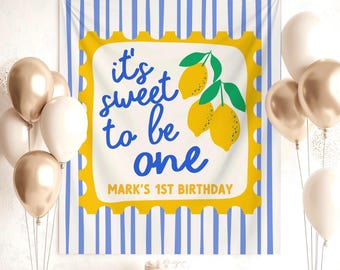 May include: A birthday party scene with a banner that reads "It's sweet to be one" with lemon illustrations. Gold and white balloons, wrapped gifts, and a cake are also present. The banner has blue and white stripes.