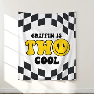 May include: White wall tapestry with a black and white checkered border. The center features the text "GRIFFIN IS TWO COOL" in yellow and black, with a smiley face and lightning bolts.