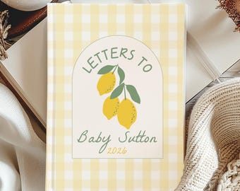 May include: A hardback journal with a yellow gingham pattern. The cover features the text "Letters to Baby Sutton 2026" with a lemon illustration. The journal is open on a white surface with other decorative items.