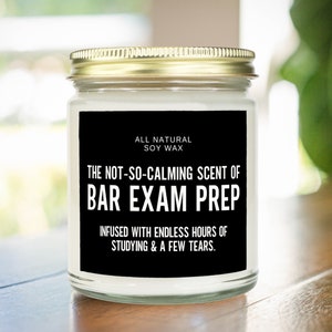 May include: A black and white candle jar with a gold lid. The label reads "ALL NATURAL SOY WAX THE NOT-SO-CALMING SCENT OF BAR EXAM PREP INFUSED WITH ENDLESS HOURS OF STUDYING & A FEW TEARS."