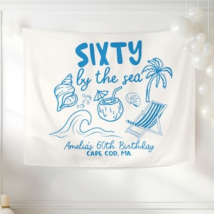 Może przedstawiać: Biały baner z tkaniny z niebieskim tekstem i ilustracjami. Na banerze widnieje napis "SIXTY by the sea" z obrazami muszli, fali, napoju kokosowego, palmy i leżaka. Tekst "Amelia's 60th Birthday CAPE COD, MA" jest również dołączony.