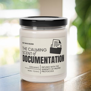 May include: A white candle jar with a black lid and a label that reads "The Calming Scent of Documentation". The label also says "Soy Wax Blend", "Organic", "Non-Toxic", "Infused with the Serenity of Proper Protocols", and has a black icon of a file folder with a document inside.