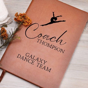 May include: A brown leather journal with the text "Coach Thompson Galaxy Dance Team" and a silhouette of a gymnast in mid-air.