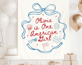 Puede incluir: Una pancarta de tela blanca con un diseño de cinta azul y el texto "Olivia is One American Girl" en rojo. La pancarta incluye ilustraciones de un globo, gafas de sol, una magdalena, fuegos artificiales y una bandera estadounidense.