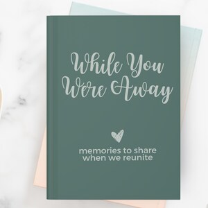 May include: A green journal with the text "While You Were Away" and "memories to share when we reunite" in white. A small heart is in the center of the journal.