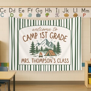 May include: A white banner with green stripes, featuring a camping theme. The banner reads "Welcome to Camp 1st Grade" and "Mrs. Thompson's Class". The banner has a graphic of a tent, mountains, trees, and a campfire.