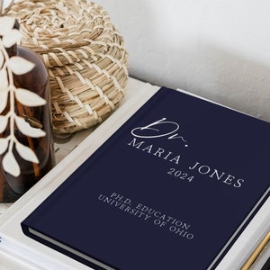 Puede incluir: Un diario de tapa dura de color azul marino con el texto "Dr. Maria Jones 2024" y "Ph.D. Education University of Ohio" en letras blancas.