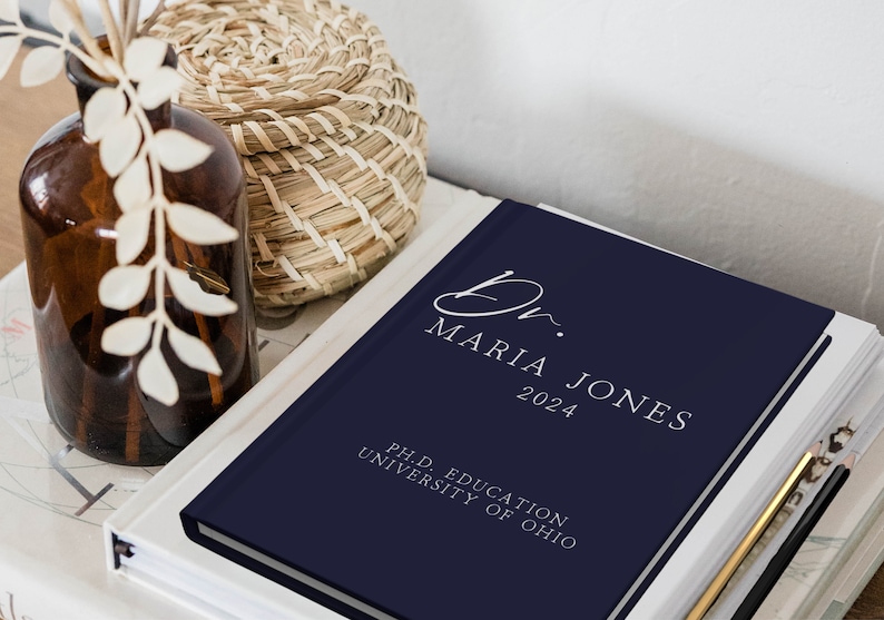Puede incluir: Un diario de tapa dura de color azul marino con el texto "Dr. Maria Jones 2024" y "Ph.D. Education University of Ohio" en letras blancas.
