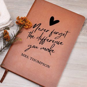 May include: A brown leather journal with the text "Never forget the difference you make" and a small heart symbol. The name "MRS. THOMPSON" is printed below the text.