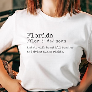 Puede incluir: Camiseta blanca con la palabra "Florida" impresa en negro, junto con una definición. La definición dice: "Un estado con hermosas playas y derechos humanos moribundos."