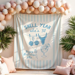 Könnte beinhalten: Ein rechteckiger Stoffhintergrund mit hellblauen vertikalen Streifen auf cremefarbenem Grund. Der Text "SHELL YEAH she's 30" und "Happy Birthday, Allie" ist in Blau gedruckt, ergänzt durch Illustrationen eines Muschel-Bikinis und eines Cocktails.