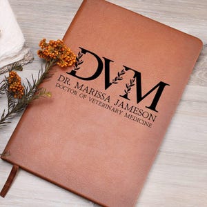 May include: A brown leather journal with the text "DVM Dr. Marissa Jameson Doctor of Veterinary Medicine" in black lettering.