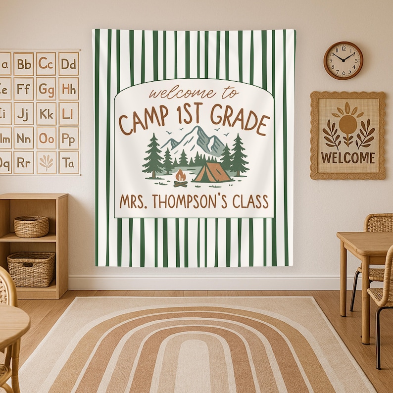 May include: A green and white striped banner with the text "Welcome to Camp 1st Grade" and "Mrs. Thompson's Class". The banner features a cartoon illustration of a campsite with a tent, trees, and a campfire.