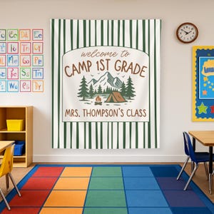 May include: A white and green striped banner with the text "welcome to CAMP 1ST GRADE" in brown lettering. The banner also includes a campfire, tent, and mountains in a green and brown color scheme. The text "MRS. THOMPSON'S CLASS" is printed below the main text.