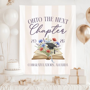 May include: A graduation banner with the text "ONTO THE NEXT Chapter 2026" in a script font. The banner features an open book with a graduation cap and floral arrangement. The banner also includes the text "CONGRATULATIONS, AMANDA".