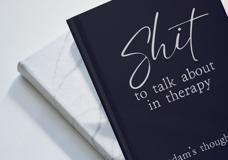 Op de afbeelding: Twee hardcover boeken. E&eacute;n is zwart met witte tekst die luidt: "Shit to talk about in therapy". Het andere boek is wit met een marmerpatroon. De boeken staan schuin naar elkaar toe.