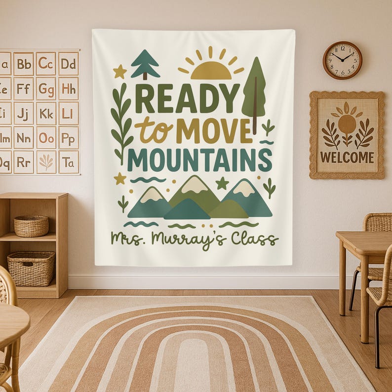 May include: A white tapestry with green mountains, a yellow sun, and the text "READY to MOVE MOUNTAINS" in brown lettering. The text "Mrs. Murray's Class" is written below the mountains.