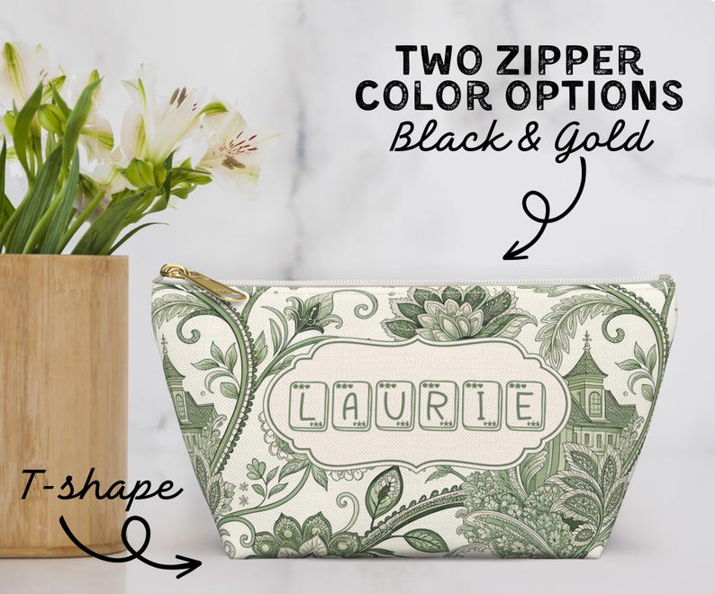 K&ouml;nnte beinhalten: Eine T-f&ouml;rmige Kosmetiktasche mit goldenem Rei&szlig;verschluss, mit einem gr&uuml;n-wei&szlig;en Blumen- und Architekturdesign. Der Name "LAURIE" ist auf der Vorderseite abgebildet. Der Text oben lautet "TWO ZIPPER COLOR OPTIONS Black & Gold."