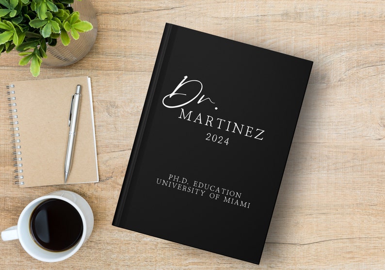Puede incluir: Diario de tapa dura negro con texto blanco que dice "Dr. Martinez 2024" y "Ph.D. Education University of Miami".