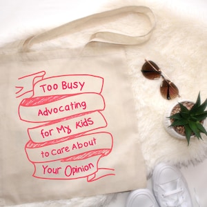 May include: A white canvas tote bag with a pink design that says "Too Busy Advocating for My Kids to Care About Your Opinion".