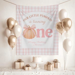 Op de afbeelding: Een verjaardagssc&egrave;ne met een banner met de tekst "Our Little Pumpkin is turning one" en een pompoenillustratie. Gouden, witte en transparante ballonnen zijn gerangschikt. Een taart en cadeaus staan op een tafel.