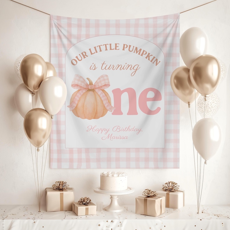 Op de afbeelding: Een verjaardagssc&egrave;ne met een banner met de tekst "Our Little Pumpkin is turning one" en een pompoenillustratie. Gouden, witte en transparante ballonnen zijn gerangschikt. Een taart en cadeaus staan op een tafel.