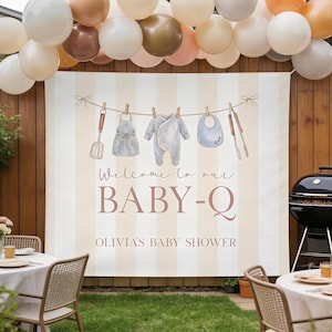 May include: A baby shower banner with a striped background and the text "Welcome to our BABY-Q, Olivia's Baby Shower." The banner features illustrations of baby clothes and grilling tools hanging on a clothesline, with balloons overhead.