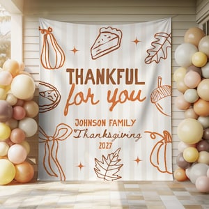 Op de afbeelding: Een rechthoekige stoffen achtergrond met een verticaal gestreept patroon in wit en lichtbeige. De tekst luidt THANKFUL for you, JOHNSON FAMILY, Thanksgiving, 2027. Illustraties bevatten oranje omlijningen van pompoenen, taart, bladeren en een eikel.