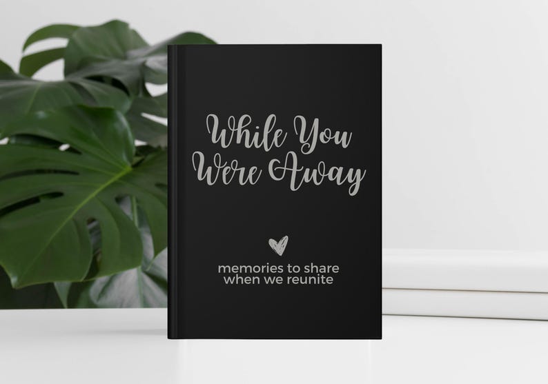 May include: Black journal with the text "While You Were Away" in silver lettering. A small heart symbol is below the text, and the words "memories to share when we reunite" are below the heart.