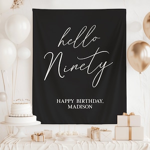 May include: A black backdrop with the words "hello Ninety" in elegant white script, with "HAPPY BIRTHDAY, MADISON" below. The scene includes white and gold balloons, a cake, and wrapped gifts, creating a festive birthday setting.