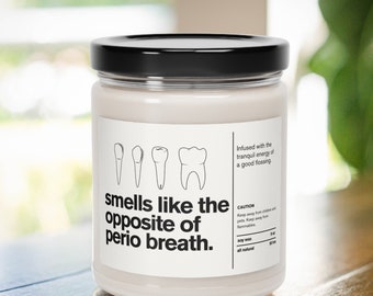 May include: A white candle jar with a black lid. The label reads "smells like the opposite of perio breath." and features a line drawing of teeth. The candle is infused with the tranquil energy of a good flossing.  The candle is made with soy wax and is all natural.