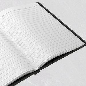 Op de afbeelding: Een open notitieboek met gelinieerde pagina's. De pagina's zijn wit met dunne grijze lijnen en een verticale margelijn. Het notitieboek heeft een zwarte kaft en binding. De afbeelding is vanuit een hoek genomen en toont de open pagina's.