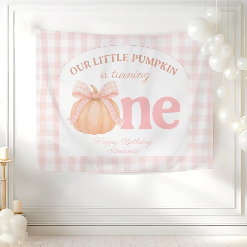 Op de afbeelding: Een roze en witte geruite achtergrond met de tekst "OUR LITTLE PUMPKIN is turning one" in een zachtroze lettertype. Een aquarel pompoen met een strik is gecentreerd onder de tekst. De woorden "Happy Birthday Amanda" staan onderaan.