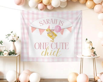 Puede incluir: Un telón de fondo rosa y blanco a cuadros con el texto "Sarah is One Cute Chick" y una ilustración de acuarela de un pollito sosteniendo un globo. El telón de fondo está decorado con banderines rosas y un arco de globos.