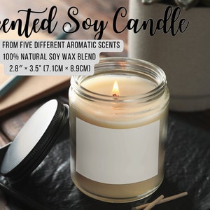 May include: A clear glass jar candle with a white label. The candle is lit and the flame is visible. The candle is on a wooden surface with a black lid and matches. The text on the label reads "Scented Soy Candle" and "CHOOSE FROM FIVE DIFFERENT AROMATIC SCENTS 100% NATURAL SOY WAX BLEND 2.8" x 3.5" (7.1CM &times; 8.9CM)"