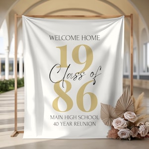 May include: A white fabric banner hanging on a wooden frame featuring the text WELCOME HOME, Class of 1986, MAIN HIGH SCHOOL, and 40 YEAR REUNION. The numbers 19 and 86 are printed in large gold font, while the remaining text is in black.