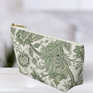 K&ouml;nnte beinhalten: Eine Kosmetiktasche mit einem gr&uuml;nen Blumenmuster auf wei&szlig;em Hintergrund. Die Tasche hat einen goldenen Rei&szlig;verschluss und eine rechteckige Form. Das Blumenmuster umfasst Bl&auml;tter, Bl&uuml;ten und Paisley-Elemente.