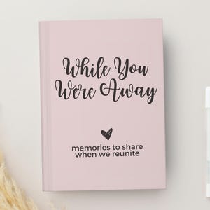 May include: A pink journal with the text "While You Were Away" and the words "memories to share when we reunite" below. A small heart symbol is between the two lines of text.