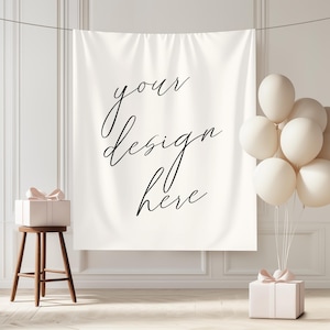 Pode incluir: Uma faixa branca com o texto "your design here" em escrita elegante está suspensa contra uma parede branca. Um pequeno banco de madeira segura uma caixa de presente com uma fita rosa, e um grupo de balões brancos.