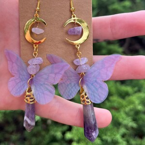 May include: A pair of gold crescent moon earrings with amethyst gemstone accents and purple butterfly charms.