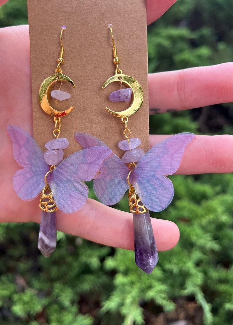 May include: A pair of gold crescent moon earrings with amethyst gemstone accents and purple butterfly charms.