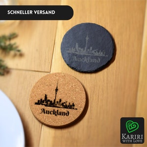 Puede incluir: Dos posavasos redondos, uno de pizarra negra y otro de corcho, con una silueta grabada con láser del horizonte de Auckland. El texto "Auckland" también está grabado en cada posavasos.