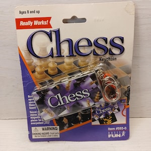 Può includere: Portachiavi a scacchi in una confezione. La confezione presenta la parola "Chess" in grandi lettere blu. Ci sono anche le parole "Really Works!" e "Ages 8 and up". Il portachiavi ha un piccolo disegno a scacchiera.