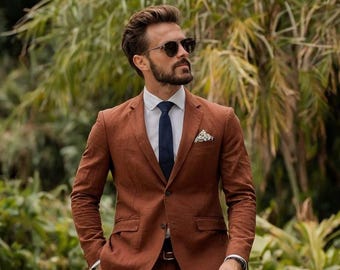 Pode incluir: Um fato castanho com camisa branca e gravata azul marinho. O fato tem um casaco de dois botões e calças a condizer. Um lenço de bolso estampado adiciona um toque de detalhe. A pessoa está a usar óculos de sol.