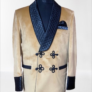 May include: A tan velvet blazer with a black quilted shawl collar and black trim. The blazer has four black buttons with a floral design and a black pocket square.